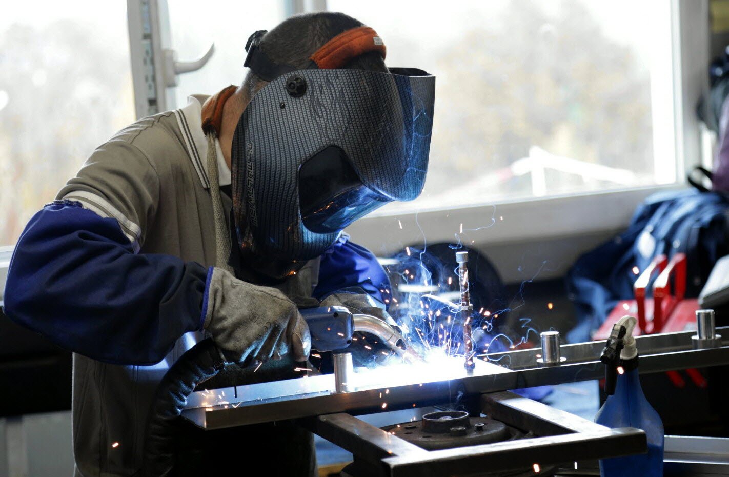 Soudeur Plimetal assemblant une pièce métallique, étincelles de soudure en atelier